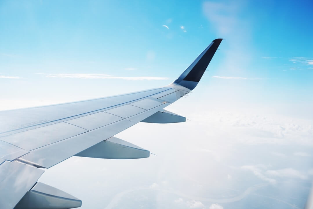 View from an airplane window showing a wing against a backdrop of blue sky and clouds.